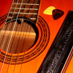 Orange, acoustic guitar with nylon strings, a harmonica and couple of picks upon it.